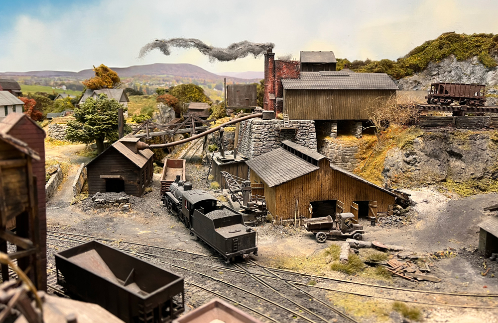  Smoke billows from the chimney of a smelter as a short steam locomotive pushes a gondola across a diamond and into the smelter complex