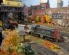 A black-and-red diesel switcher uses a flatcar to reach across a float bridge and pull cars from a rail barge