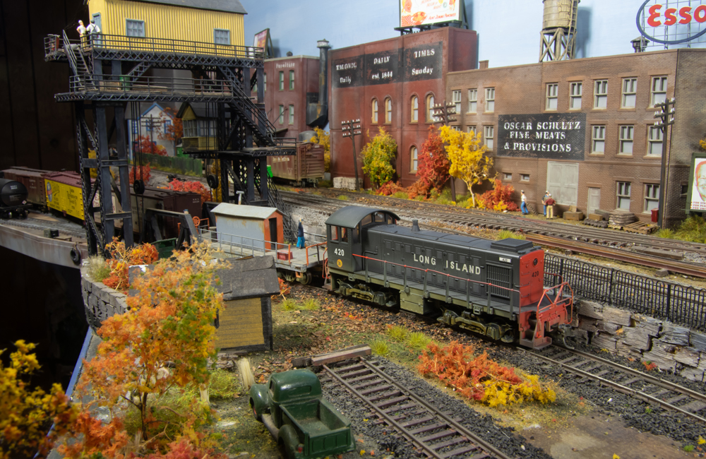 A black-and-red diesel switcher uses a flatcar to reach across a float bridge and pull cars from a rail barge