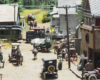 A small, black geared steam locomotive pulls a green wooden coach across a street bustling with pedestrians and horse-drawn wagons