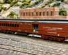 Seated figures are seen through the open door of a dark red heavyweight baggage-coach