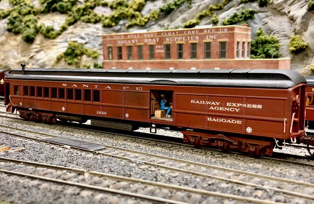 Seated figures are seen through the open door of a dark red heavyweight baggage-coach