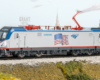 Photo of HO scale electric locomotive on scenicked base with cityscape background