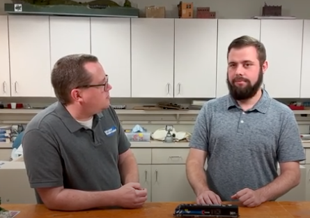 Two men speaking at a workbench.