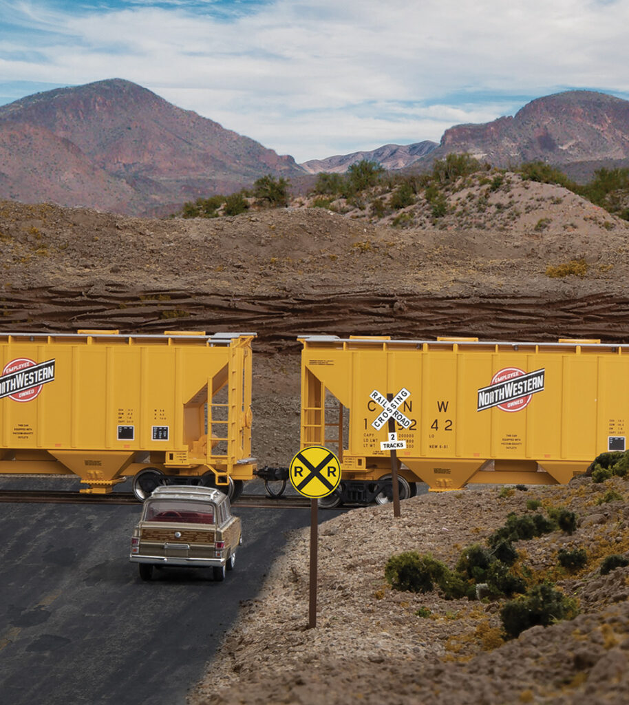 Railroad crossing sign in front of yellow hopper cars