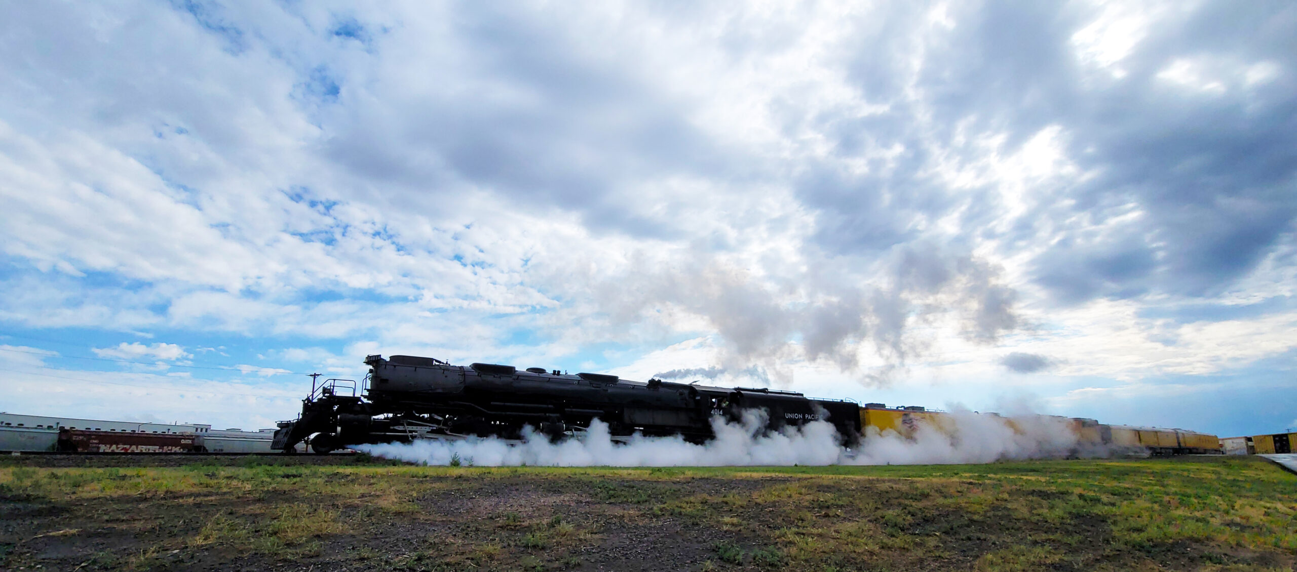 Steam shooting from a large black articulated steam locomotive as it pulls its train.