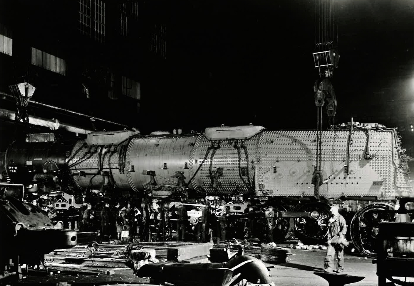 The boiler-smoker-firebox assembly of a Big Boy steam locomotive is lowered onto its wheels by an enormous interior crane.