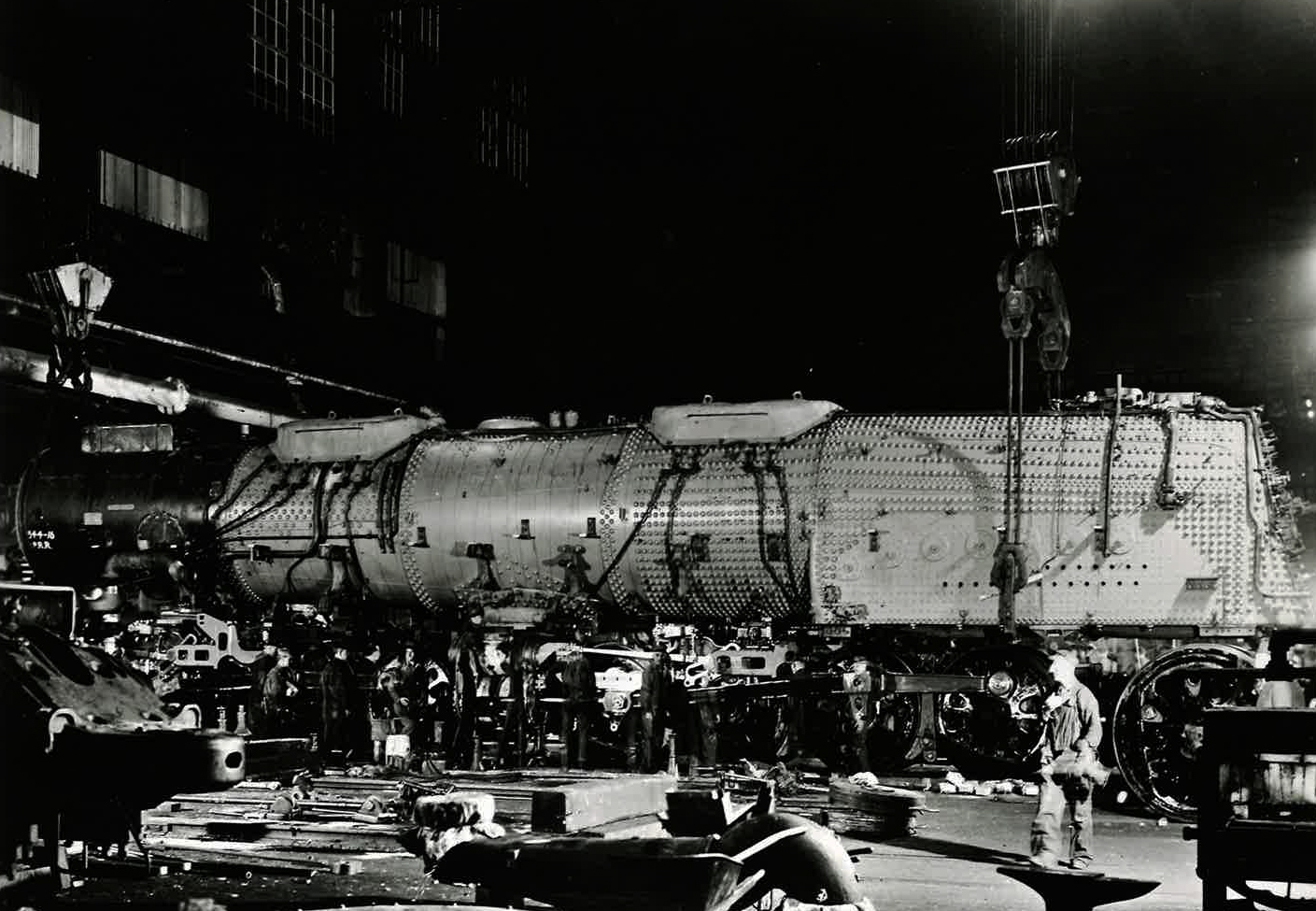 Boiler-smokebox-firebox assembly for a Big Boy steam locomotive is lowered onto its wheels with a massive indoor crane.
