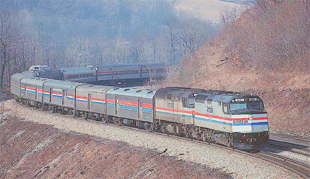red, blue and silver passenger train winding around a mountain curve.