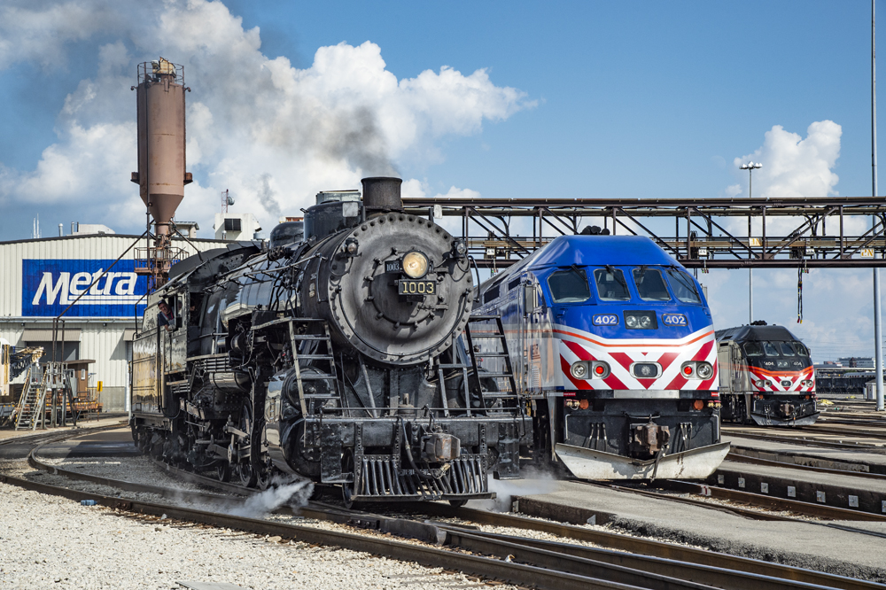 Steam locomotive next to red, white, and blue diesel