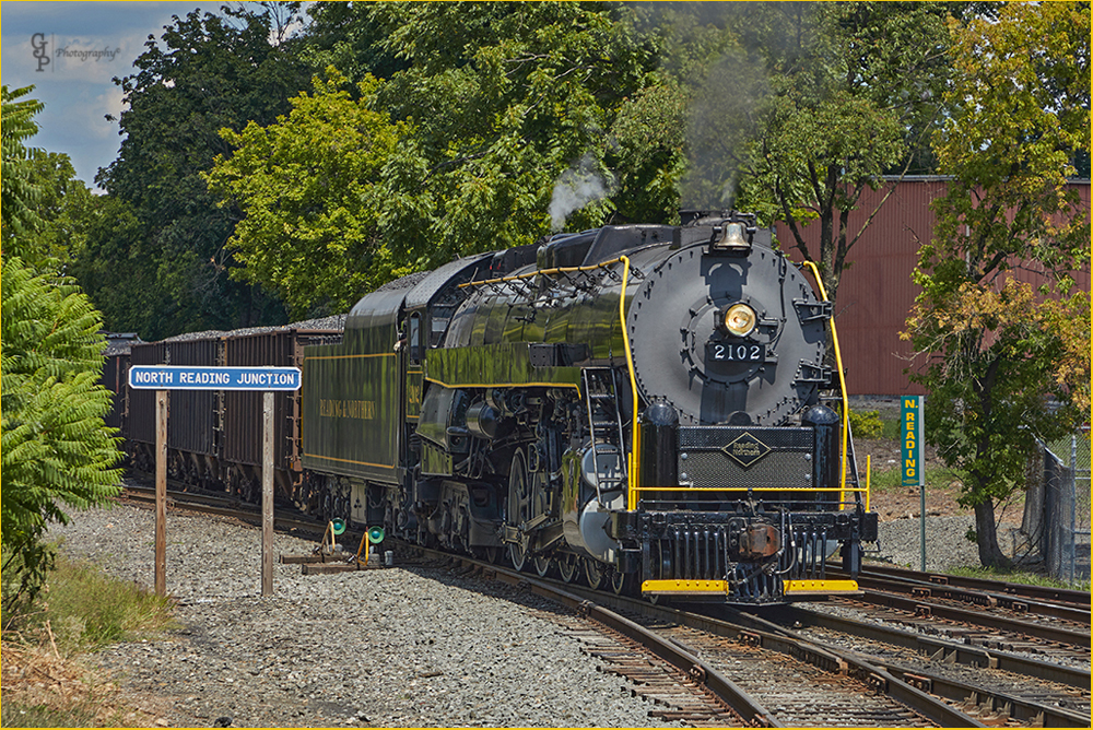 Steam locomotive passing "North Reading Junction" sign with freight train