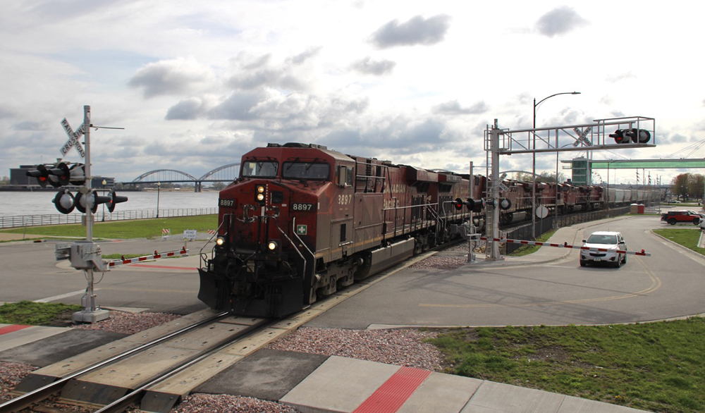 Freight train with red locomotives at grade crossing with river in background