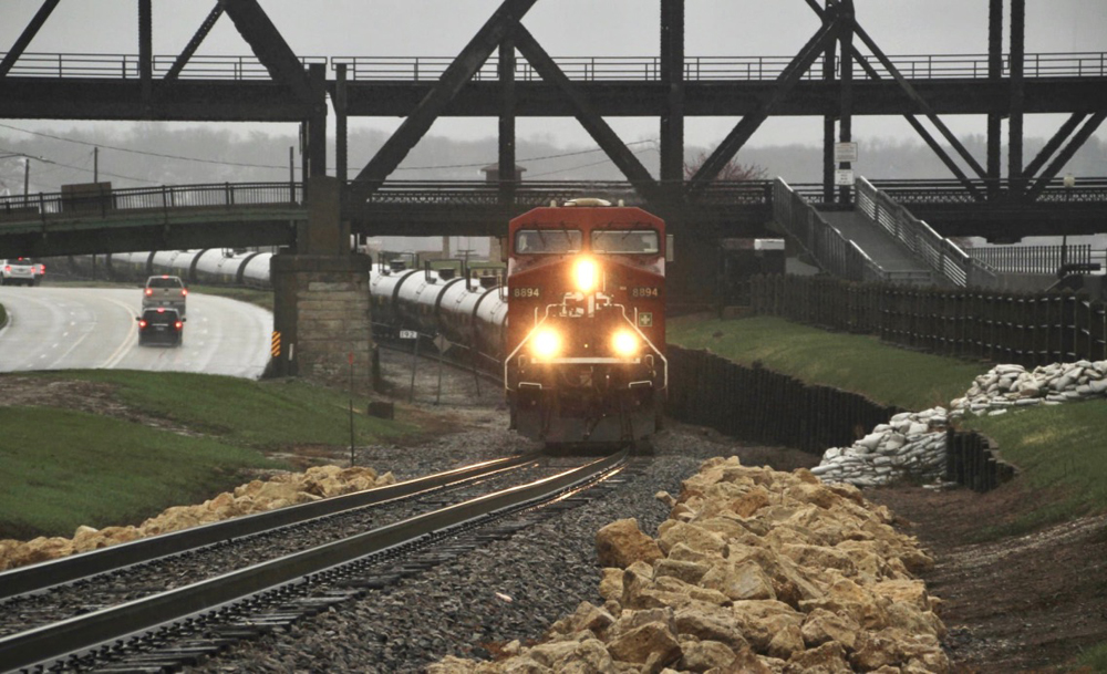 Train of tank cars curves under bridge in rainstorm