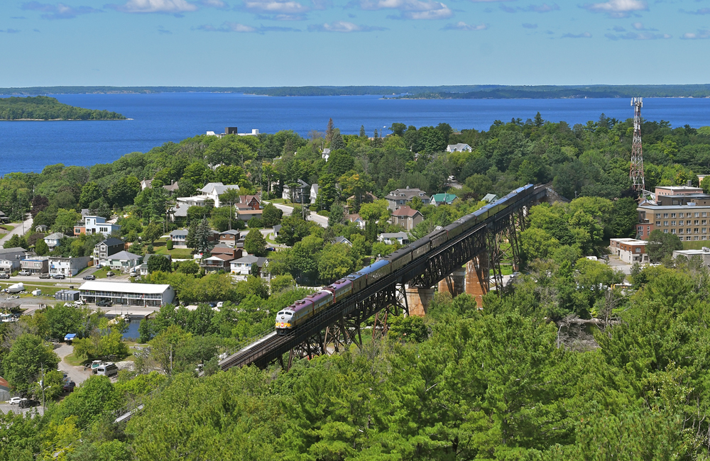 Passenger train crossing long bridge above town with lake in background