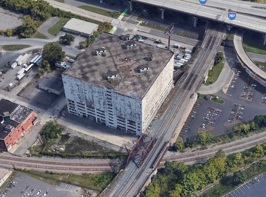 Aerial view of large square concrete building and adjacent roads and railraod tracks