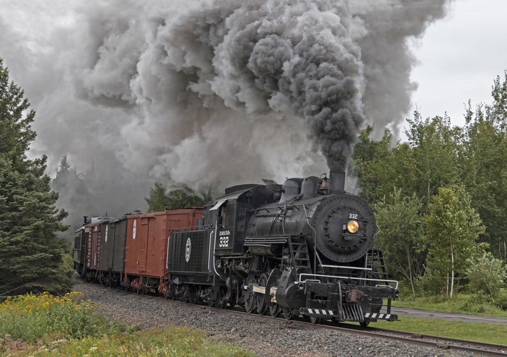 Steam locomotive with vintage freight cars under huge plume of black smoke
