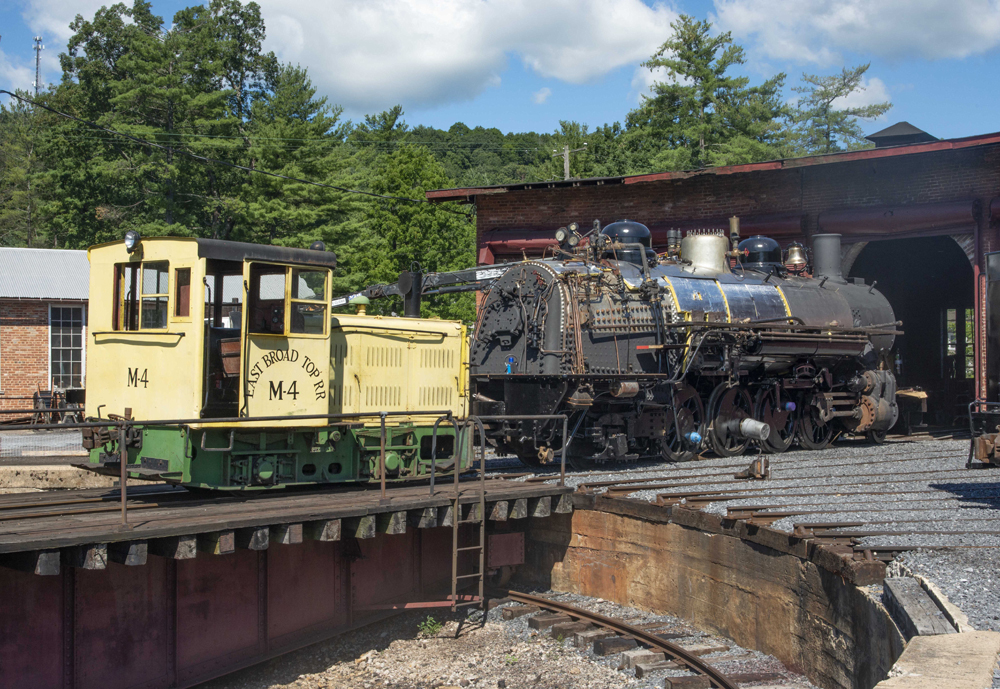 Yellow diesel switcher moves steam locomotive under restoration