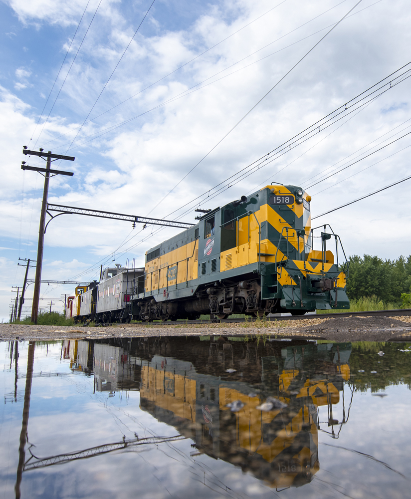 Green and yellow diesel and cabooses reflected in puddle of water