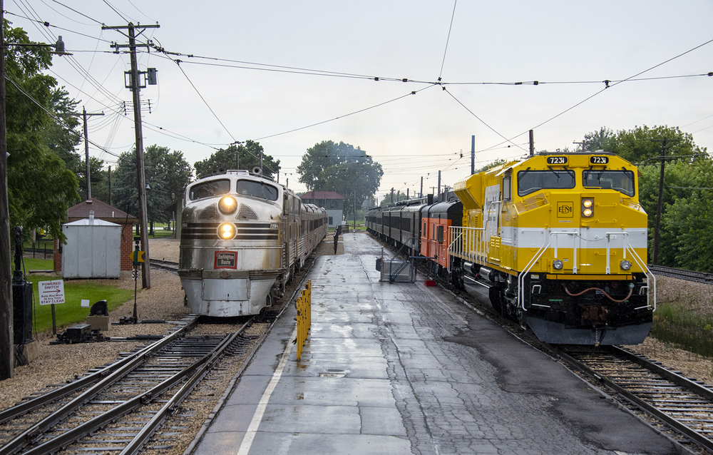 Silver passenger train passes yellow freight locomotive with older-style passenger cars