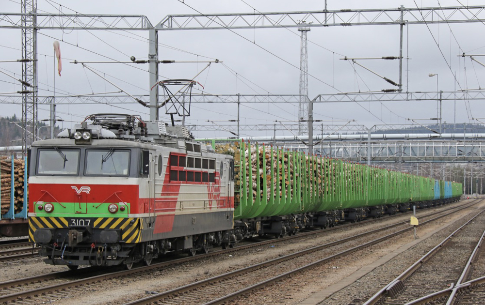 Red and white electric locomotive with green strip on nose pulling green log-carrying cars