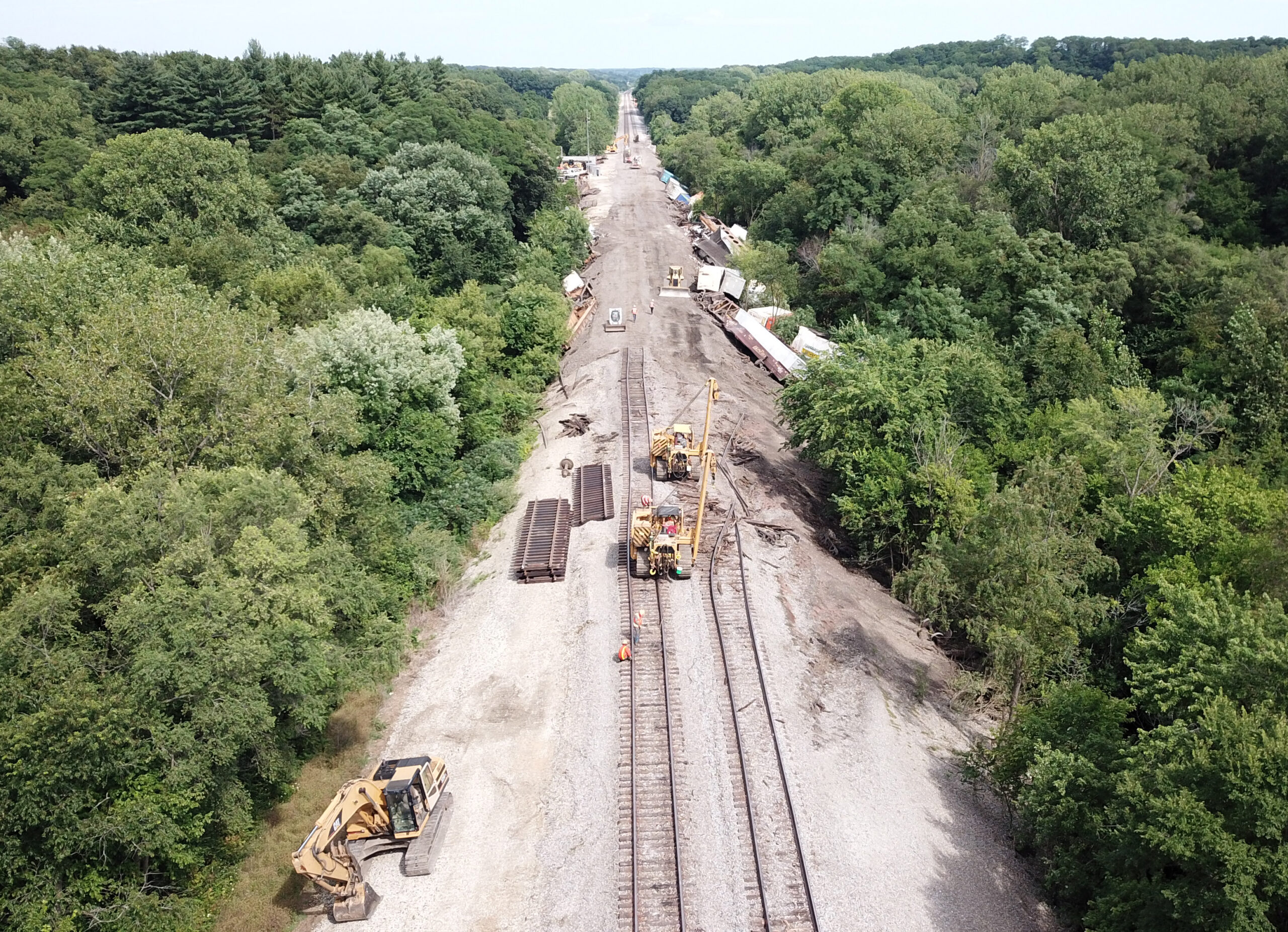 Heavy equipment working on railroad tracks with derailed cars off to one side