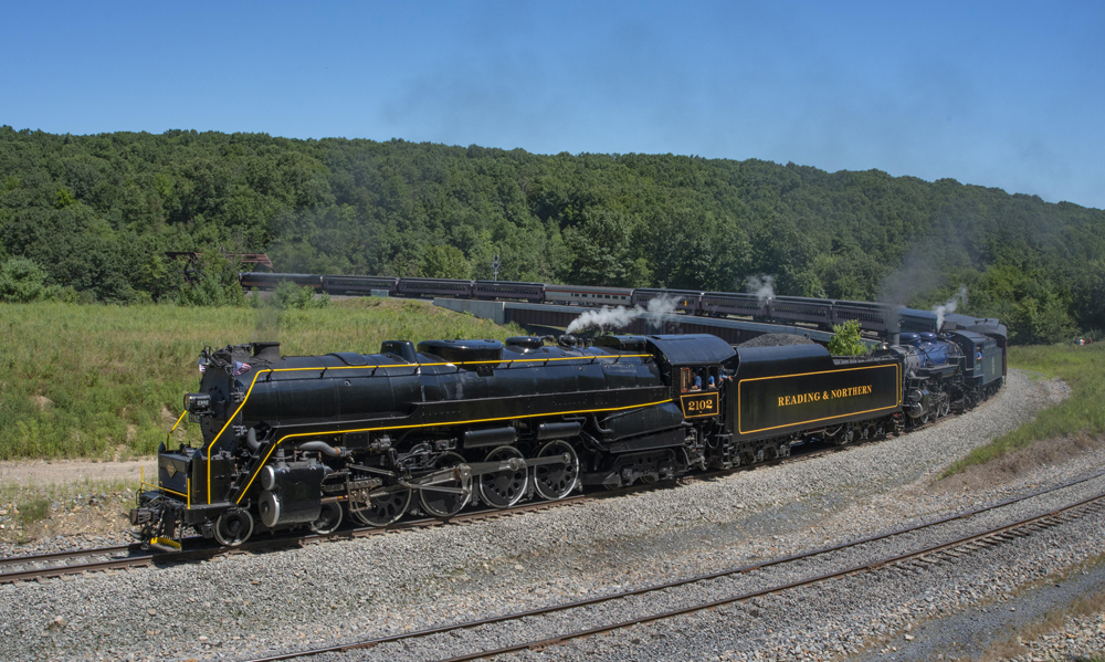 Passenger train with two steam locomotives rounds sharp curve