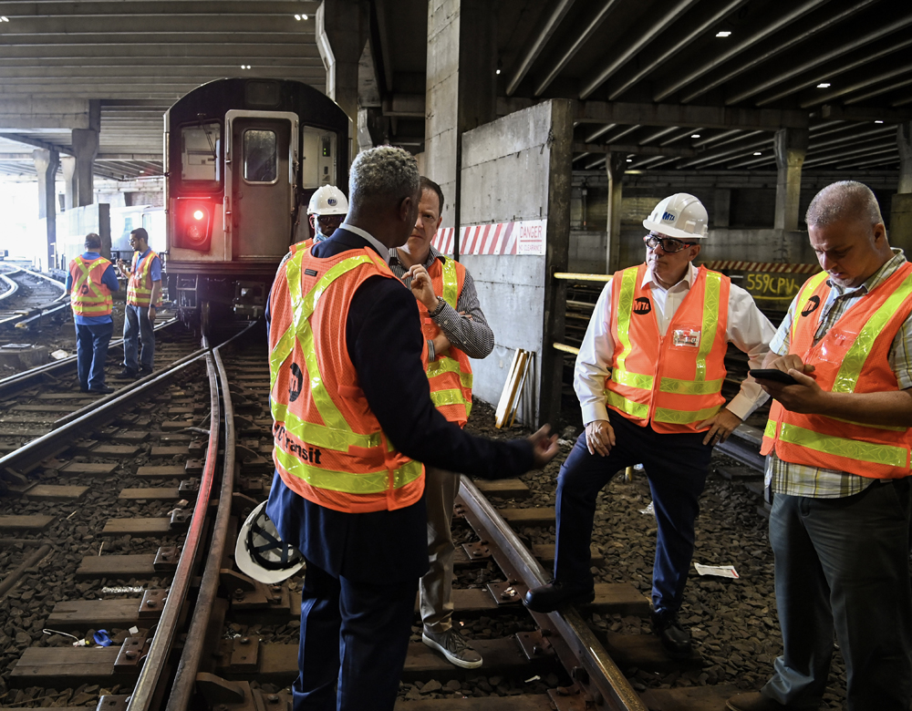 Men in high-visibility vests and hard hats talking at subway yard
