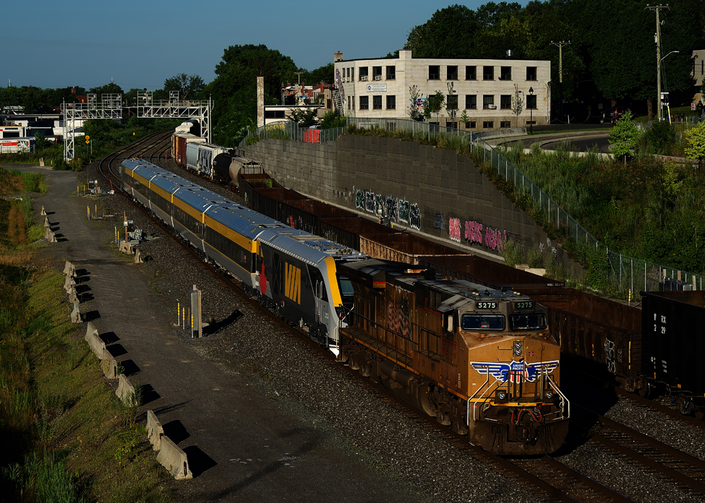 Yellow freight locomotive with passenger train in tow
