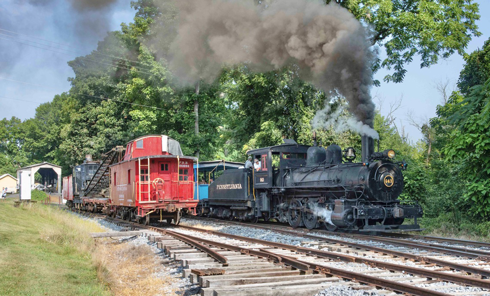 Steam engine passes caboose on adjacent track
