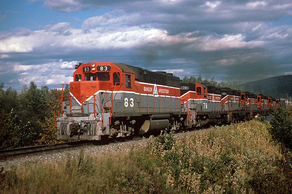 Six red, gray, and black diesel Bangor Aroostook locomotives on train in wilderness