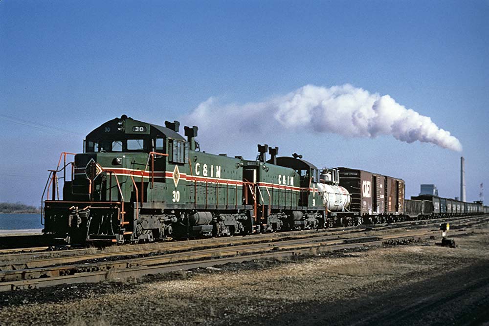 Green and red diesel locomotives with freight train in yard
