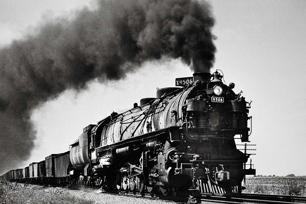 Smoking 1940s steam locomotive approaching with freight train