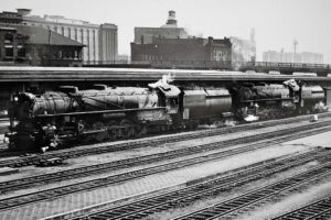 Two steam locomotives on passenger train in station