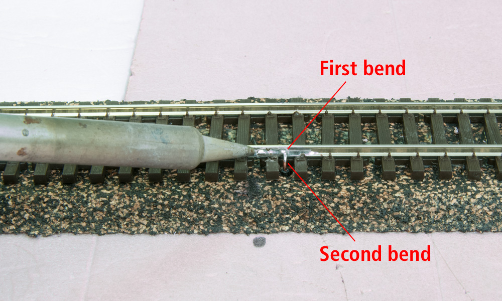 A soldering iron melts a solder joint together between a feed wire and an HO scale rail