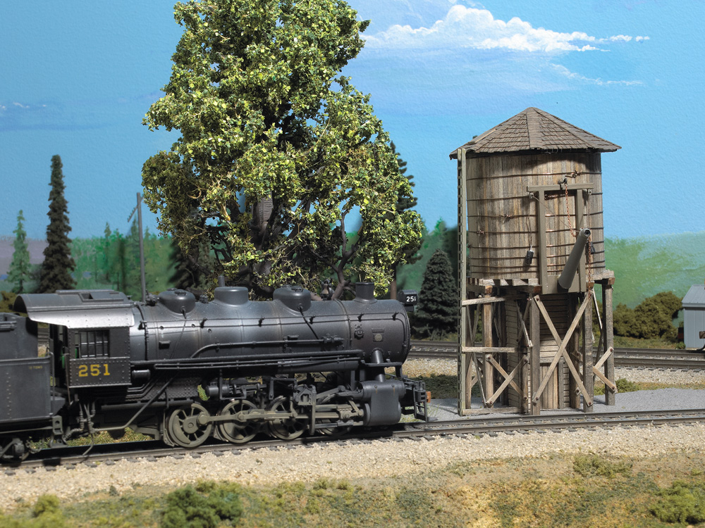 An HO scale steam locomotive approaches a wooden water tank for refilling
