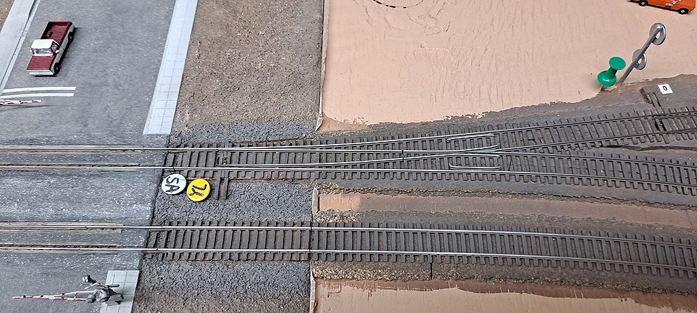 Double-track main with spur switch leading off to right on back track, adjacent to road crossing at left