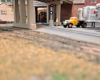 Tracks pass under highway overpass with trailer vans parked at right, red over green signal at center, with Milwaukee Road diesel emerging from tunnel through building at background