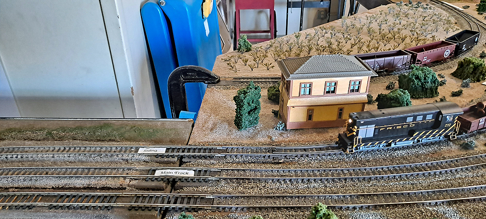 Two modular sections join with three tracks crossing connections, in background, a large C clamp is acting as a bump stop at the end of another track without a connection