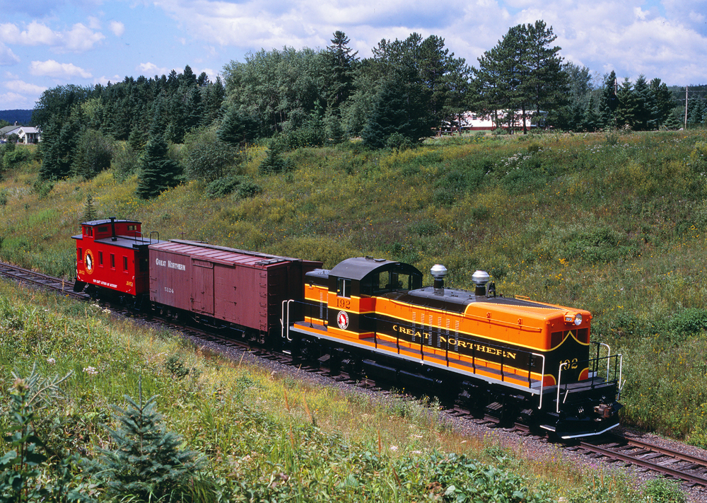 Photo of locomotive with wood boxcar and caboose in rural setting