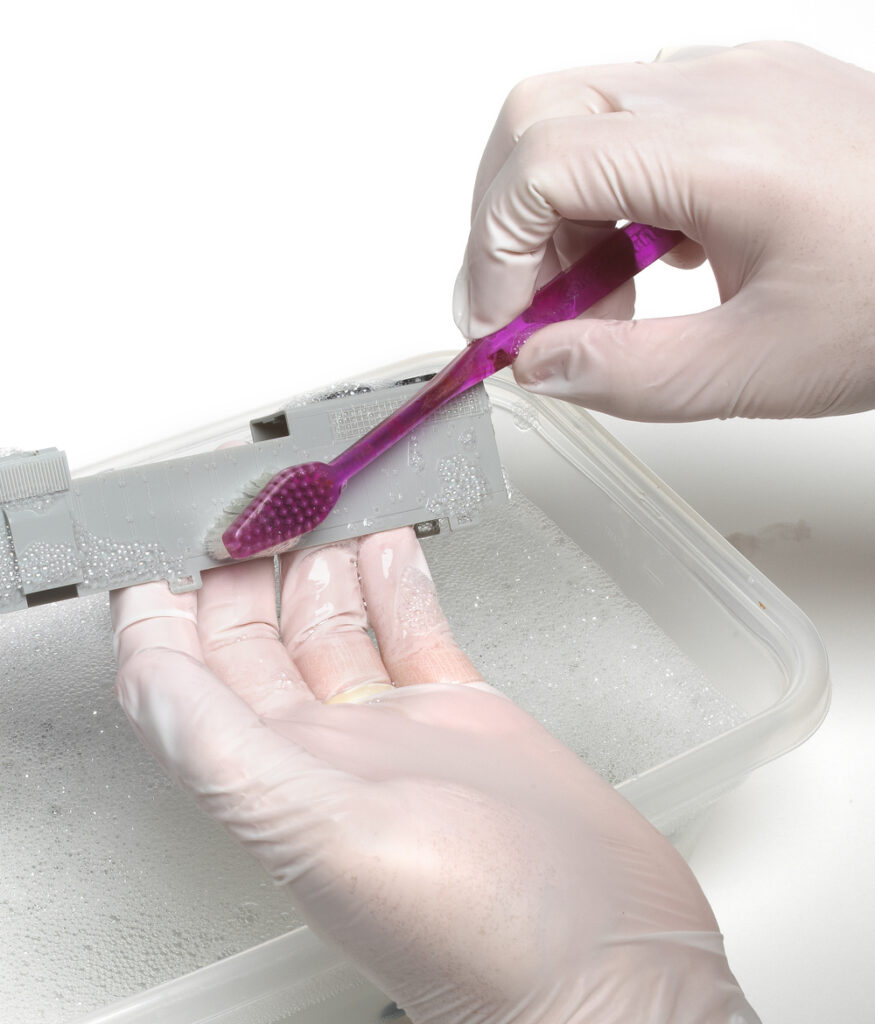 hands with toothbrush cleaning plastic model with water and soap