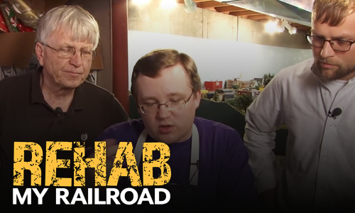 Men at a model railroad layout, with logo.