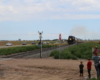 Family taking pictures as black steam locomotive approaches crossing.