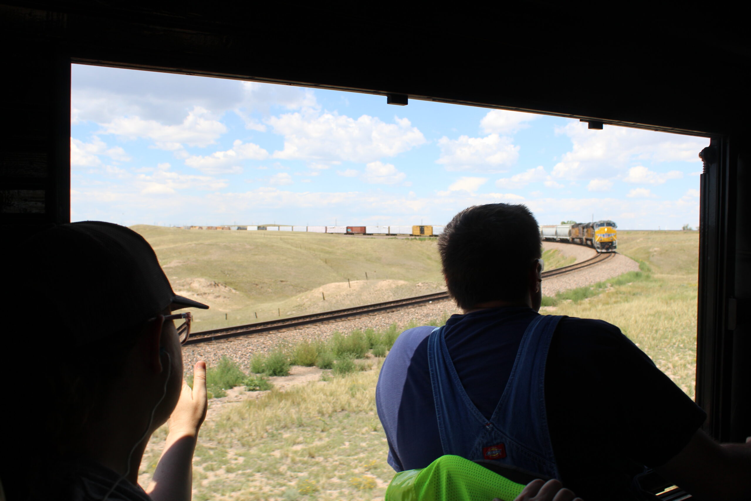 Fireman silhouetted in Big Boy cab window with diesel freight train waiting in background.