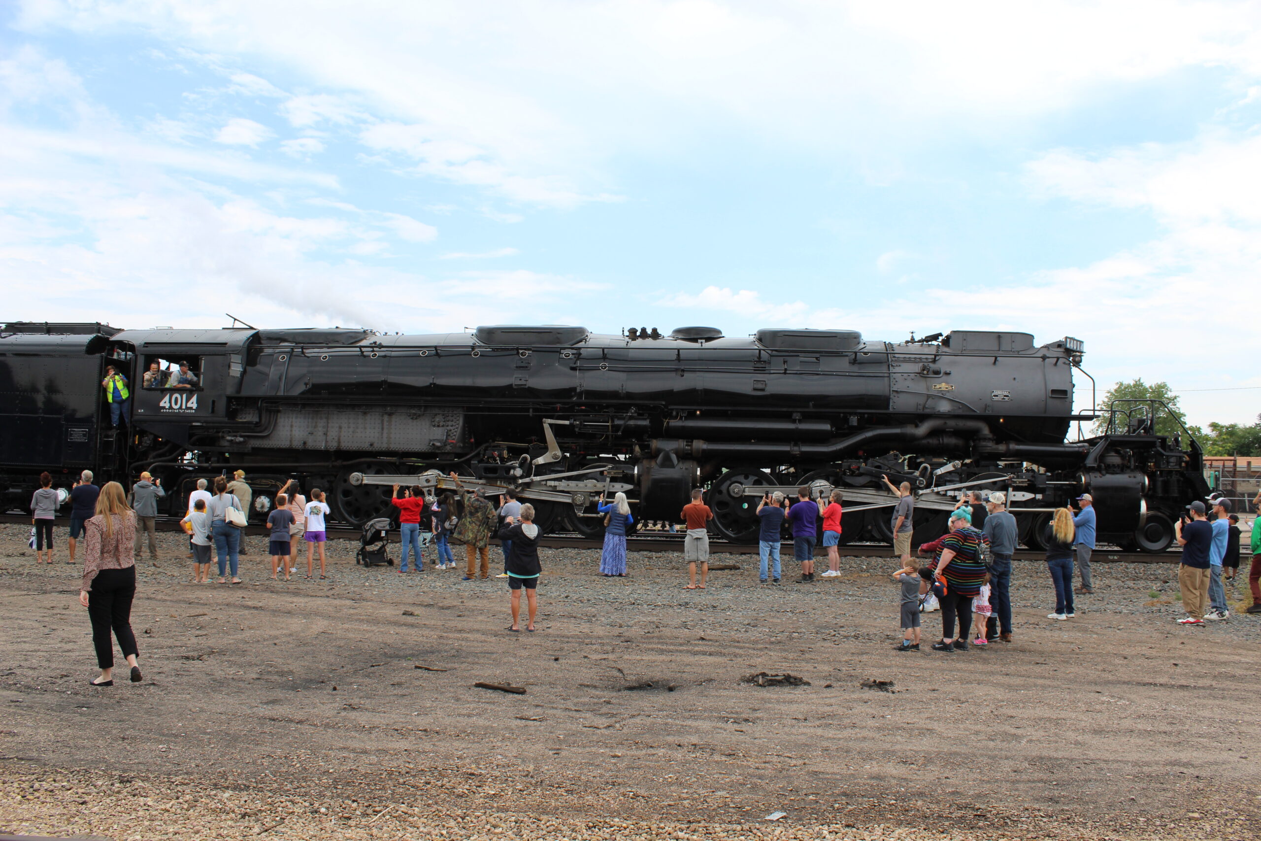 Side view of large black steam locomotive with a few people photographing it.