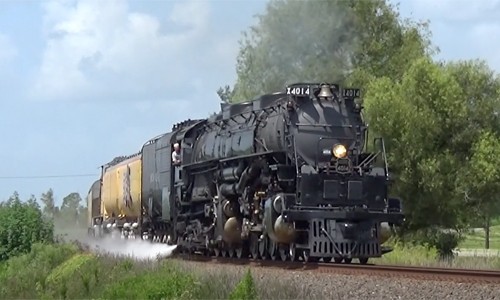 Big Boy locomotive moving a train through a curve in a lush landscape.