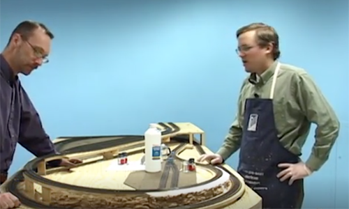 Two men on either side of a model train layout under construction.