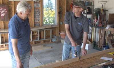 Two men talking over wood in a garage