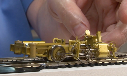 Hand guiding a brass rolling chassis of a model locomotive.