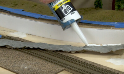 Glue gun point releaing caulk onto the back of a piece of model layout scenery rocks.