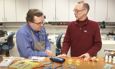 Two men talking behind a table full of modeling tools.